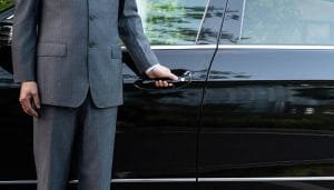 unrecognizable well dressed male chauffeur opening a car door A black limousine stands parked outside a large building, suggesting a nearby limo rental near Newark NJ