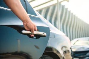 A person is opening the door handle of a black car for luxury airport transportation.