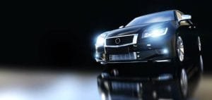 A black car shines in the dark with its headlights on, showcasing options for black car rentals.