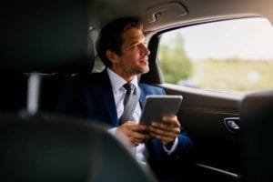 Businessman in a corporate limousine using a tablet while seated in the back seat.