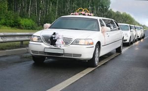 A wedding limousine adorned with a wedding cake on the back, promoting a Wedding Limo Service.