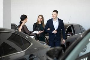 A man and woman stand together in a luxury car dealership, discussing options for a rental service.