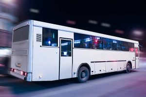A white party bus driving down the street at night, illuminated by streetlights.