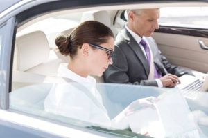 Inside a corporate event limo, a man and woman collaborate on a laptop while seated in the car.