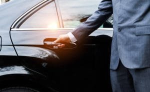 A man in a suit holds the door handle of a car, representing a professional limo rental service.