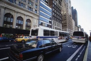 A bus and a corporate event limo parked on a busy city street, surrounded by buildings and pedestrians.