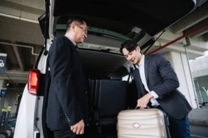Limo Rental Service Two men in business attire stand beside a car with luggage, promoting a limo rental service.